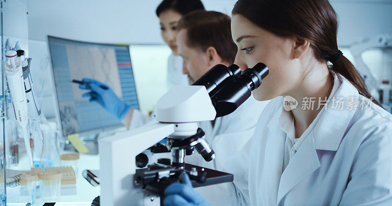 Female microbiologist during research. Using microscope. Team working in background